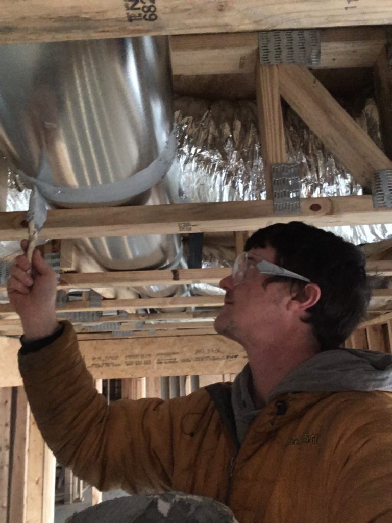 ben tatum, a maced new energy intern, stands on a ladder while sealing an air duct in eastern kentucky.