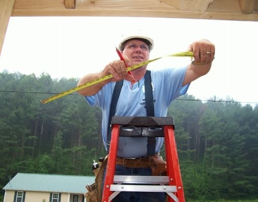 A man stands on a ladder holding a measuring tape while building a house for Frontier Housing in Eastern Kentucky.
