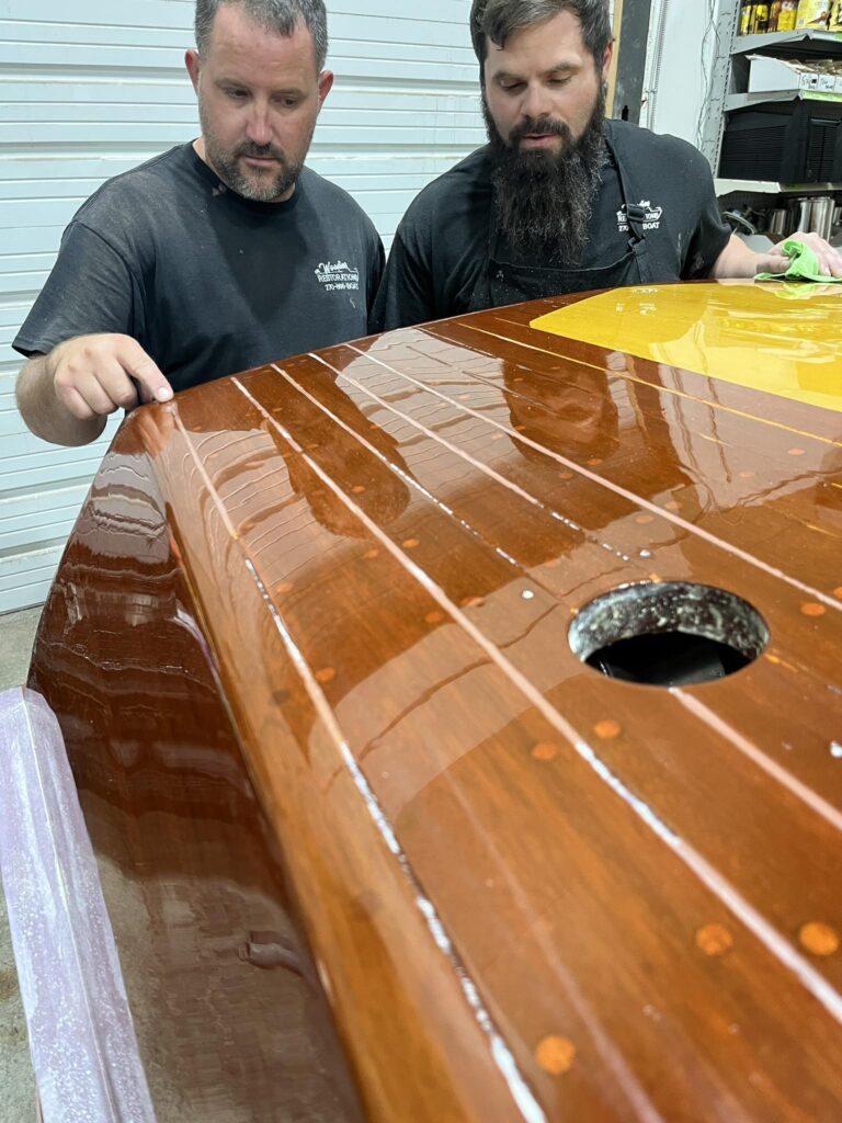 Taylor Cundiff stands with another restoration specialist as they work on repairing a boat